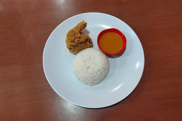 Crispy chicken, chili sauce and white rice on a white plate on the dining table