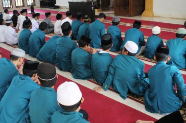 Müslüman öğrenciler camide oturup dinliyorlar.