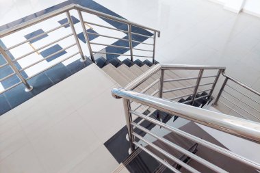 Beyaz seramik fayansları ve paslanmaz çelik tırabzanı olan kapalı merdiven.