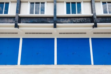 Mavi kapıları ve siyah-beyaz dış duvarları olan modern üç katlı bir bina, parlak mavi bir gökyüzünün altında..