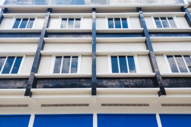 Mavi kapıları ve siyah-beyaz dış duvarları olan modern üç katlı bir bina, parlak mavi bir gökyüzünün altında..