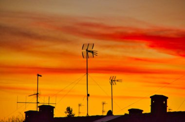 Televizyon antenlerinin silueti renkli bir günbatımında evlerin çatılarında.