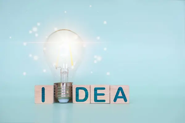 light bulb between wooden block with the words Idea on blue background, innovative and inspirational new concept