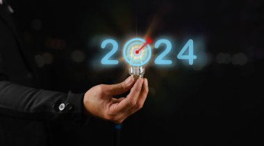 Siyah arka planda ampul tutan iş adamı, 2024 için hedefler belirleme kavramı