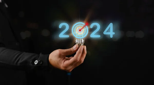 Siyah arka planda ampul tutan iş adamı, 2024 için hedefler belirleme kavramı