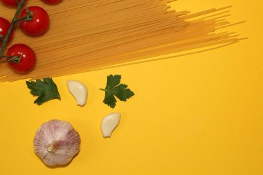 Sarı arka planda çiğ spagetti, sarımsak, bitki ve domateslerden oluşan bir yemek