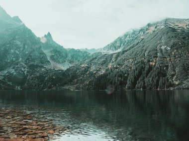 Gökyüzünün zirveleri öptüğü yerde, sakin bir göl, dağ heybetinin özünü beşikte saklar. Hafif sis dağın zirvesinde uzanıyor..