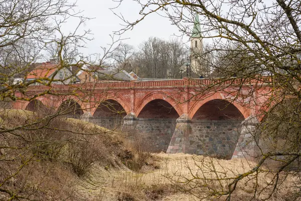 Venta Nehri 'nin sakin sularında Kuldiga' nın ikonik kırmızı tuğla köprüsünden geçmek, her adımın zamanda bir yolculuk olduğu yerden
