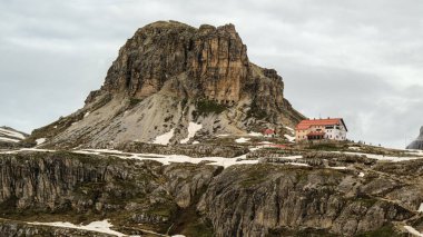 Karlı Tre Cime Pisti Dolomite zirveleriyle dolup taşan haziran sisi arasından yükseliyor