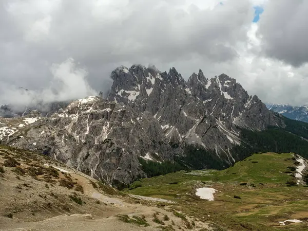 stock image Hiking through snow on Tre Cime Circuit: Dolomite peaks creating a dramatic contrast against the June fog