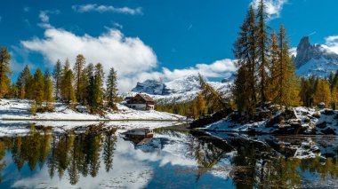 Vibrant autumn hues from the surrounding forest mirror perfectly in the calm waters of Lago Federa, with Rifugio Palmieri nestled against the backdrop of the stunning Dolomite peaks. clipart