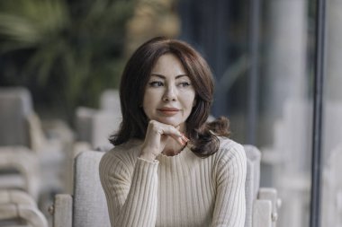 Az makyajlı bir kadının portresi. Çenesini eline dayamış ve nazikçe yan tarafa bakıyor. Hafif bir gülümsemeyle..