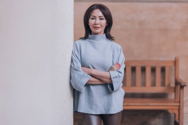 Güzel ve zarif beyaz kadın kameraya bakıyor ve gülümsüyor. Antik bir avluda taş bir sütuna yaslanıyor..