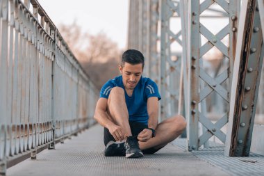 Genç sporcu, bağcıklarını dışarıda demir bir köprüde bağlıyor, spor konsepti..