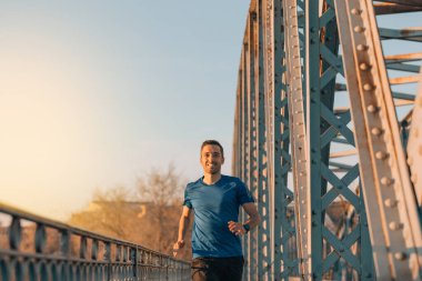 Gün batımında eski bir metal köprüde koşan genç bir sporcunun yakın çekimi, spor konsepti..