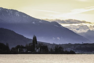 Gün batımı dağların üzerinde, kilise ve gölün önünde