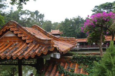 Önünde kırmızı bir çatı ve mor bir ağaç olan bir bina. Binanın etrafında bir sürü insan dolaşıyor.