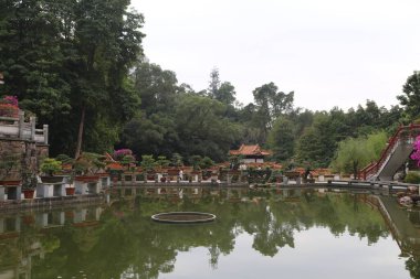 Ortasında bir çeşme ve üzerinde bir köprü olan bir gölet. Gölet ağaçlar ve bitkilerle çevrili.