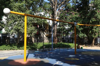 Sarı direkli ve mavi-beyaz oyun parkı olan bir oyun alanı. Bir kişi yerde oturuyor.