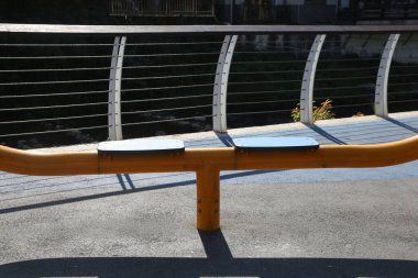 Beton bir yüzeyde sarı ve siyah bir bank var. Nehrin üzerindeki bir köprüde.