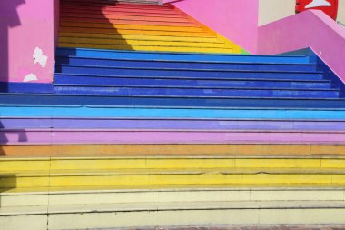 Gökkuşağı desenli renkli bir merdiven. Merdivenler farklı renklere boyanmış, canlı ve neşeli bir atmosfer yaratıyor.