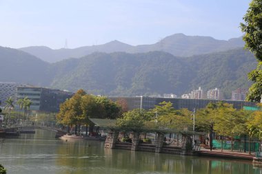 Altında nehir akan ve arkasında dağlar olan bir şehir. Şehir ağaçlar ve binalarla dolu.