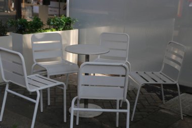 Dört sandalyesi ve masası olan beyaz bir teras. Sandalyeler sıraya dizildi, bir sandalye önde, diğer üçü de yan yana.