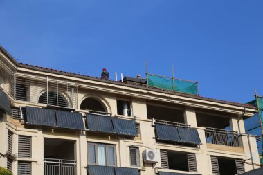 Arka planda mavi gökyüzü olan bir bina. Binanın yeşil bir çatısı ve mavi bir brandası var.