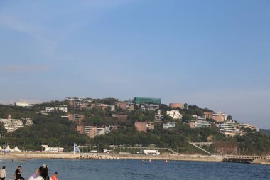 Arkasında şehir olan bir sahil. Sahil insanlarla dolu ve birçok şemsiye var.