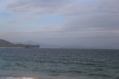 Arka planda bulutlu bir gökyüzü olan sakin bir okyanus. Gökyüzü mavi ve gri karışımı. Sahneye huzurlu ve huzurlu bir atmosfer veriyor.