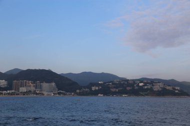Arka planda büyük bir su kütlesi olan güzel bir şehir manzarası. Gökyüzü açık ve güneş parlıyor.