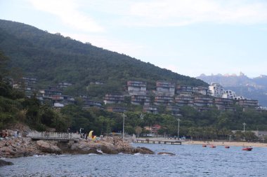 Arkasında dağ olan bir sahil. Kumsal insanlarla dolu ve suda tekneler var.