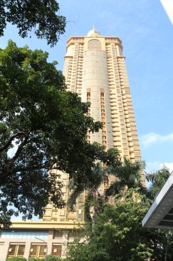 Önünde yeşil bir ağaç olan yüksek bir bina. Bina kahverengi ve bir sürü penceresi var.