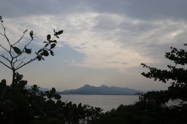 Uzakta bir dağ sırası görülebilir, ön planda bir su kütlesi ile. Gökyüzü bulutlu, karamsar bir atmosfer yaratıyor.