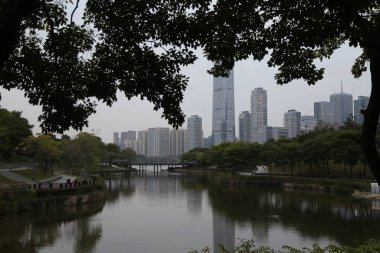 Bir şehrin ufuk çizgisi bir su kütlesine yansıyor. Su sakin ve huzurlu ve nehir kıyısında uzanan ağaçlar bir huzur hissi veriyor. Şehir aktivitelerle dolup taşıyor.