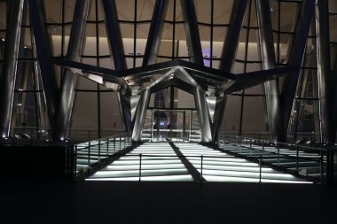 Cam girişi olan büyük bir bina. Giriş aydınlık ve parlak metalik bir görünüme sahip.