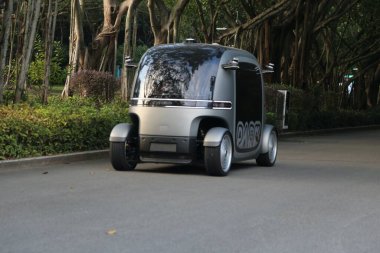 Yan tarafında siyah çizgili gümüş bir araç yoldan aşağı gidiyor. Araç kendi kendine giden bir araba.