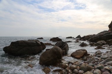 Okyanus sakin ve kayalar kıyı boyunca dağılmış. Gökyüzü bulutlu ve su koyu mavi bir renktir.