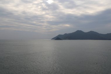 Arka planda dağ olan sakin bir okyanus. Gökyüzü bulutlu ve su koyu mavi.