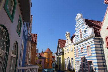 Ortasında mavi ve beyaz çizgili bir ev olan renkli binalar. Binalar yan yana dizilmiş, birlik ve uyum duygusu yaratıyorlar.