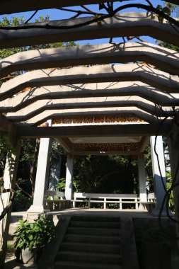 Ahşap bir yapısı ve taş merdiveni olan geniş, açık bir alan. Bina sarmaşıklarla kaplı ve çatısı var. Bölge ağaçlar ve bitkilerle çevrili.