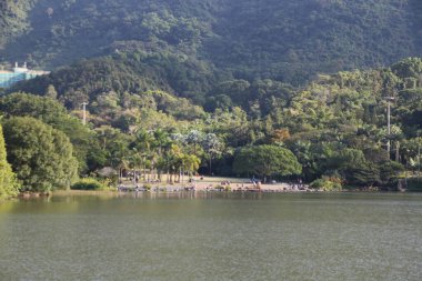 Arkasında orman olan güzel bir göl. İnsanlar manzaranın ve gölün tadını çıkarıyorlar. Manzara huzurlu ve rahatlatıcı.