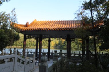 Çatı ve tırabzanı olan ahşap bir pavyon. Çadır ağaçlar ve göl ile çevrilidir.