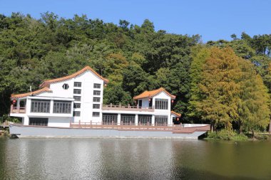 Kırmızı çatılı büyük beyaz bir ev bir gölün üzerinde oturur. Ev ağaçlarla çevrili ve su sakin. Sahnenin huzurlu ve huzurlu bir atmosferi var.