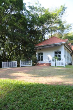 Kırmızı çatılı beyaz bir ev yemyeşil bir ormanın önünde duruyor. Ev beyaz bir çit ve beyaz bir kapı ile çevrilidir. Bahçe bir çimenlik ve birkaç saksı bitkisiyle iyi korunuyor.