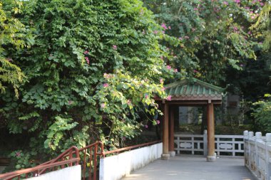 Yeşil çalılı bir yürüyüş yolu ve yeşil çatılı beyaz bir bina. Geçit bir çit ve köprü ile kaplı.