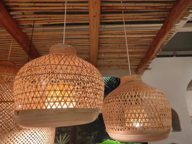 Tavandan sarkan iki ahşap lamba. Lambalar bambudan yapılmıştır ve kırsal, doğal bir görünüme sahiptir. Lambalar yanıyor, sıcak ve davetkar bir atmosfer yaratıyorlar.