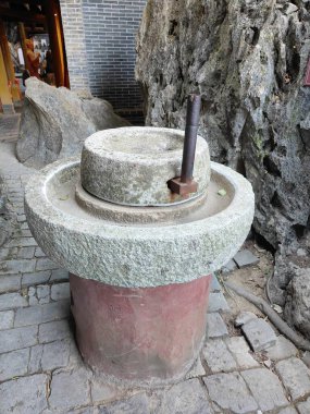 Kırmızı bir üste taştan öğütücü bir değirmen var. Değirmen kayalarla çevrili ve kırsal bir görünümü var.