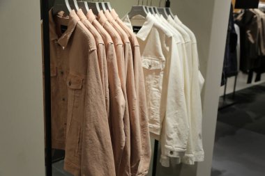 Ortasında beyaz ceket olan bir elbise askısı. Ceket beyaz, diğer ceketler bronz.