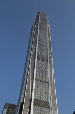 Çok yüksek bir bina ve arka planda açık mavi bir gökyüzü var. Bina o kadar yüksektir ki çevreyi kule gibi sarar. Pencereler eşit aralıklı